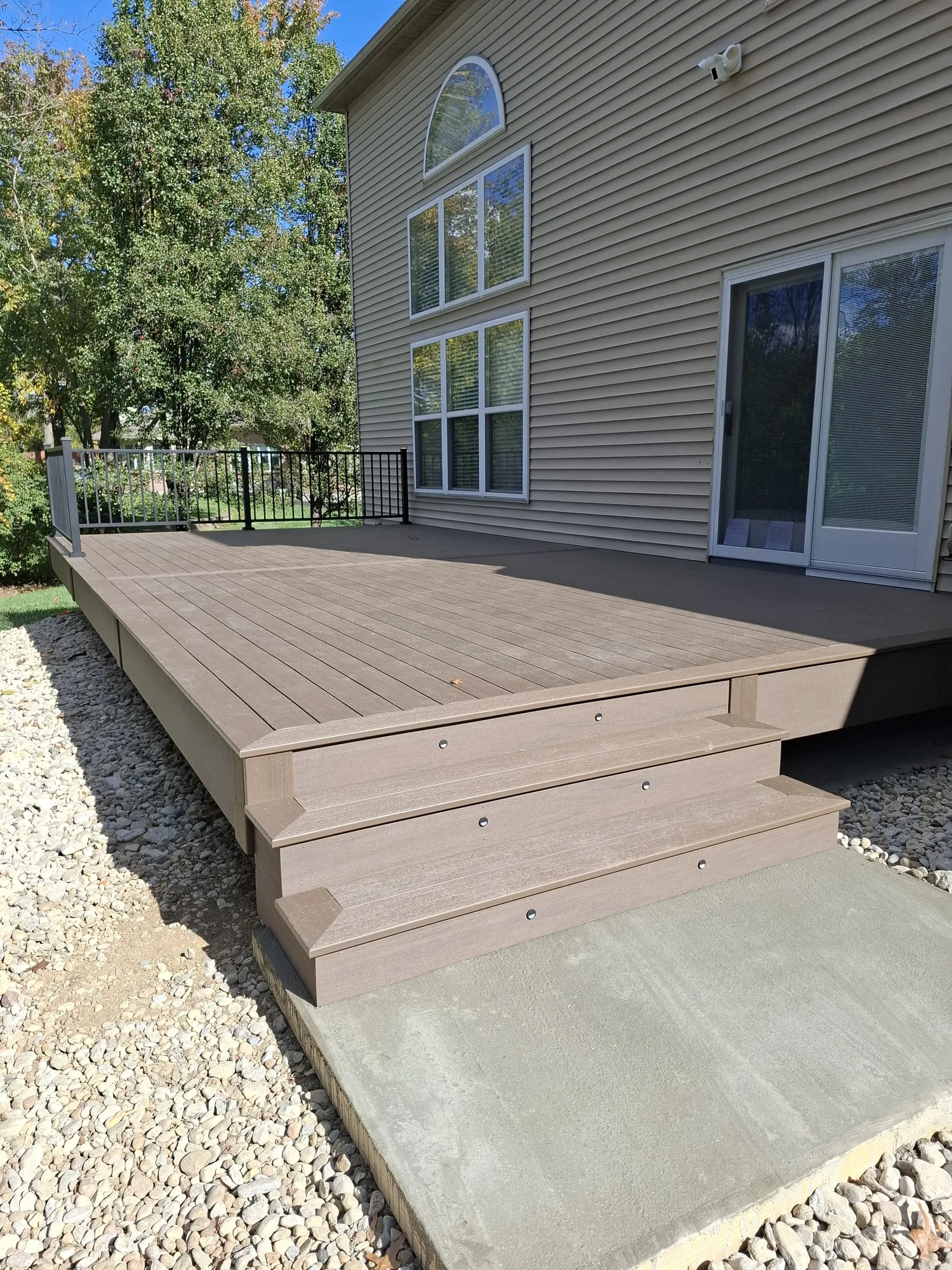 Low brown composite deck running along the back of a two story home above a concrete pad