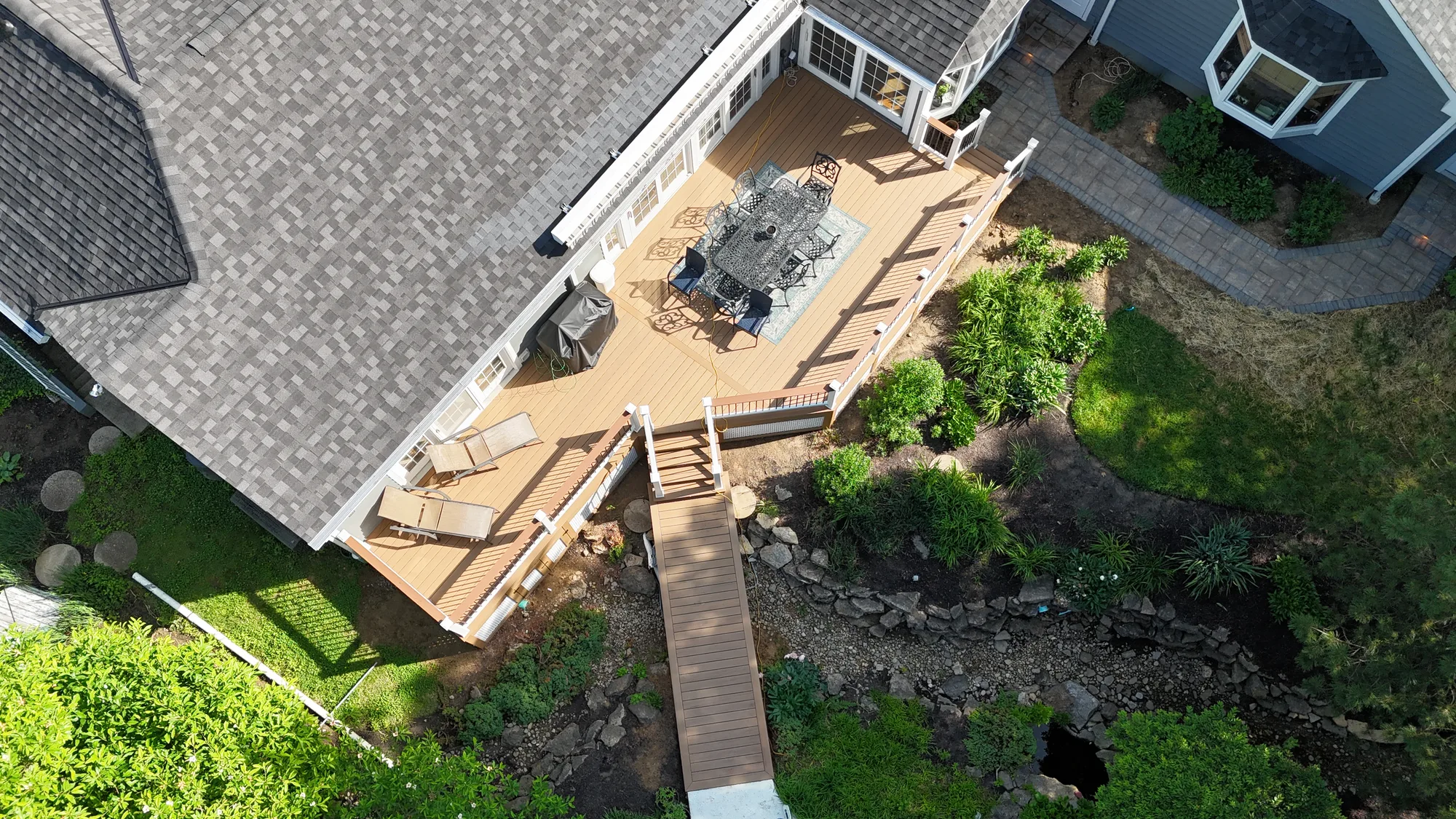 Aerial view of a paver patio with a dining set and a boardwalk style walkway through a rock garden