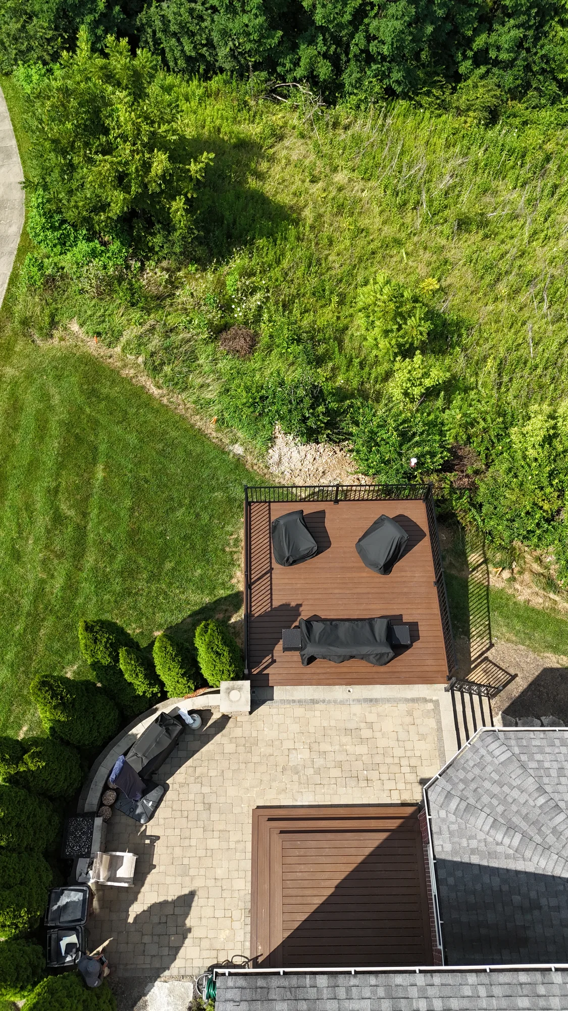 Aerial view of a small composite deck with lounge seating set on a paver patio bordered by lawn