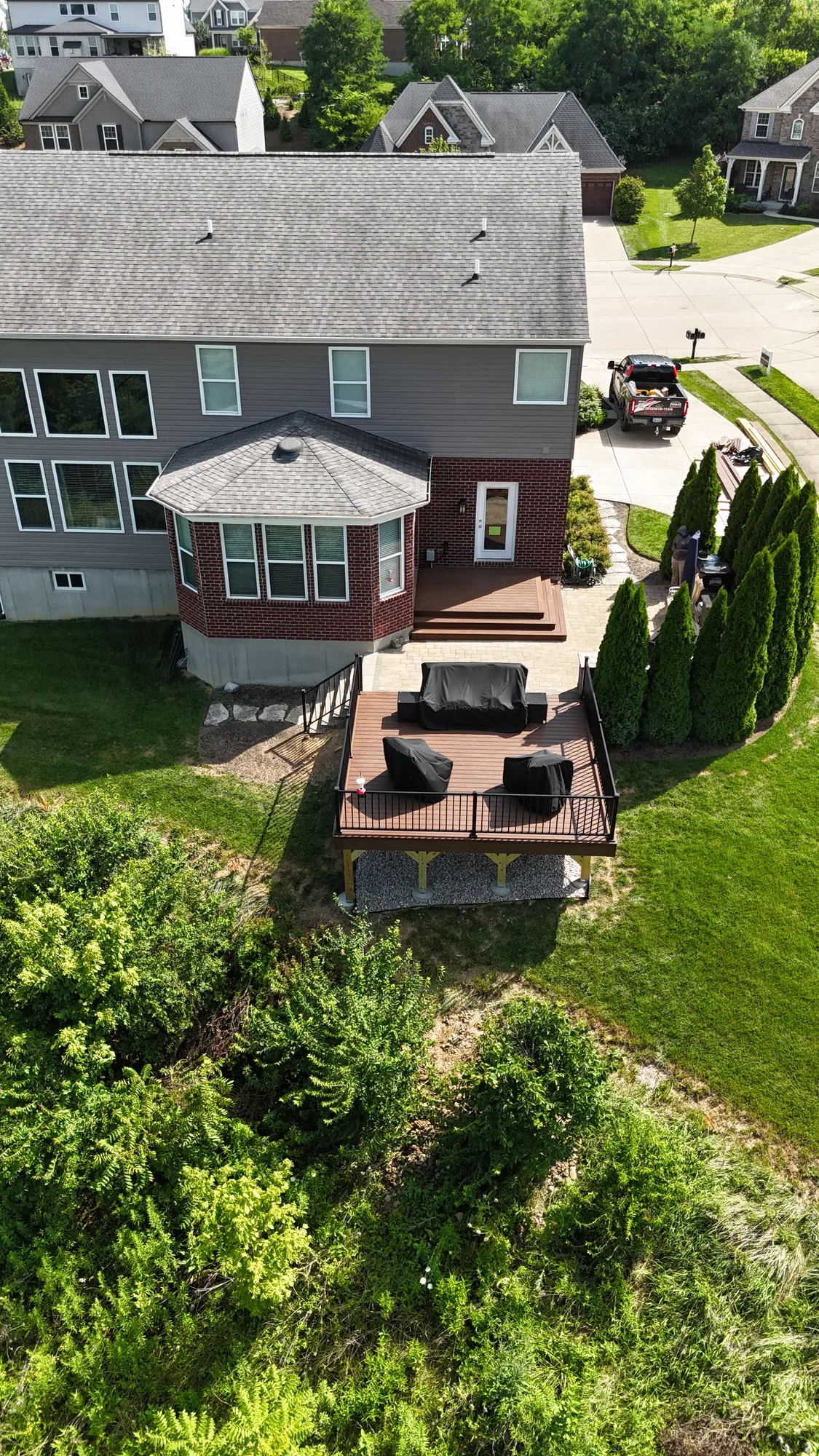 Aerial view of a two story home with a rear composite deck and lounge area in a suburban yard