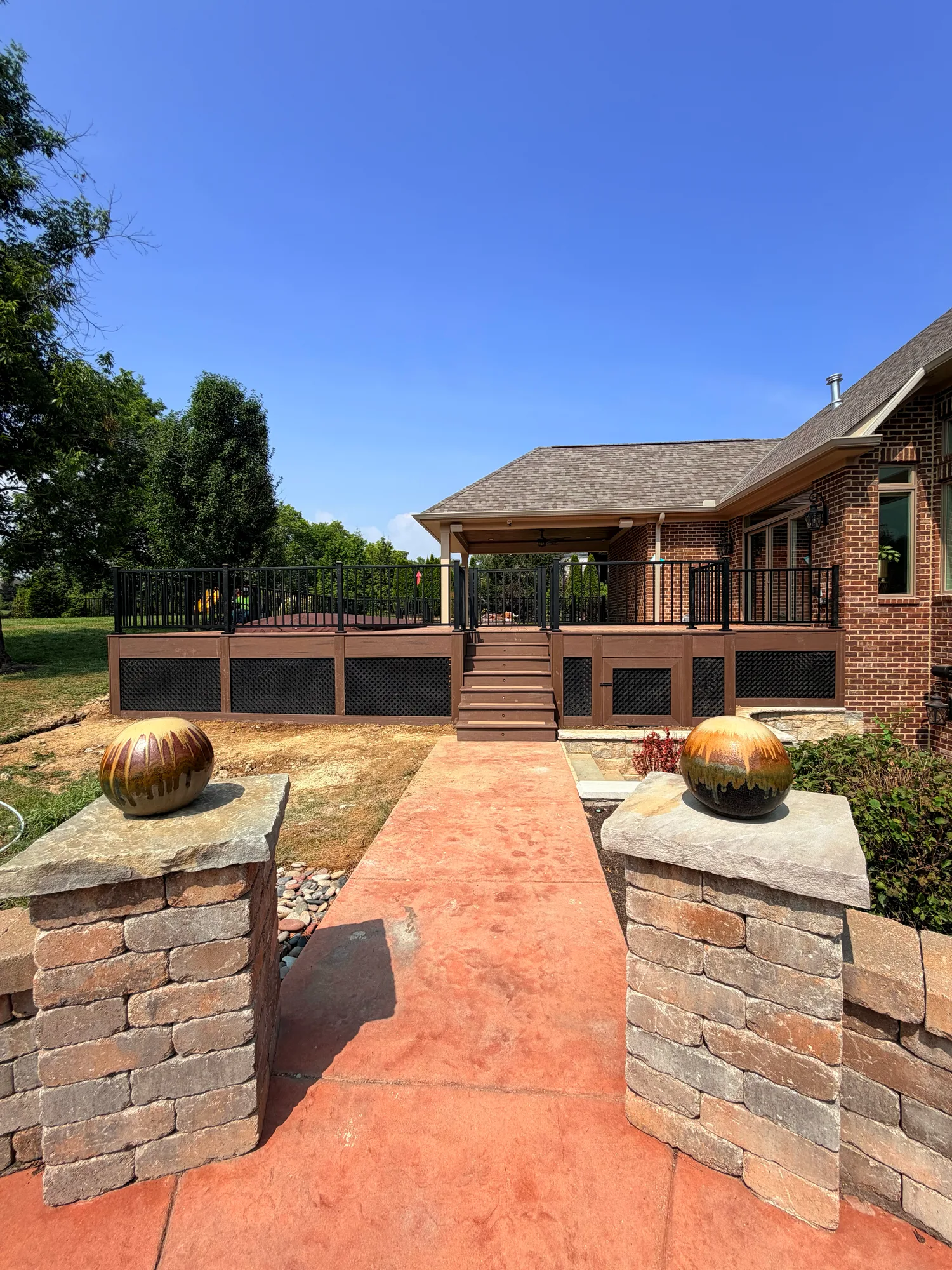 Paver walkway between stone pillars topped with copper spheres leading to a covered porch at a brick home