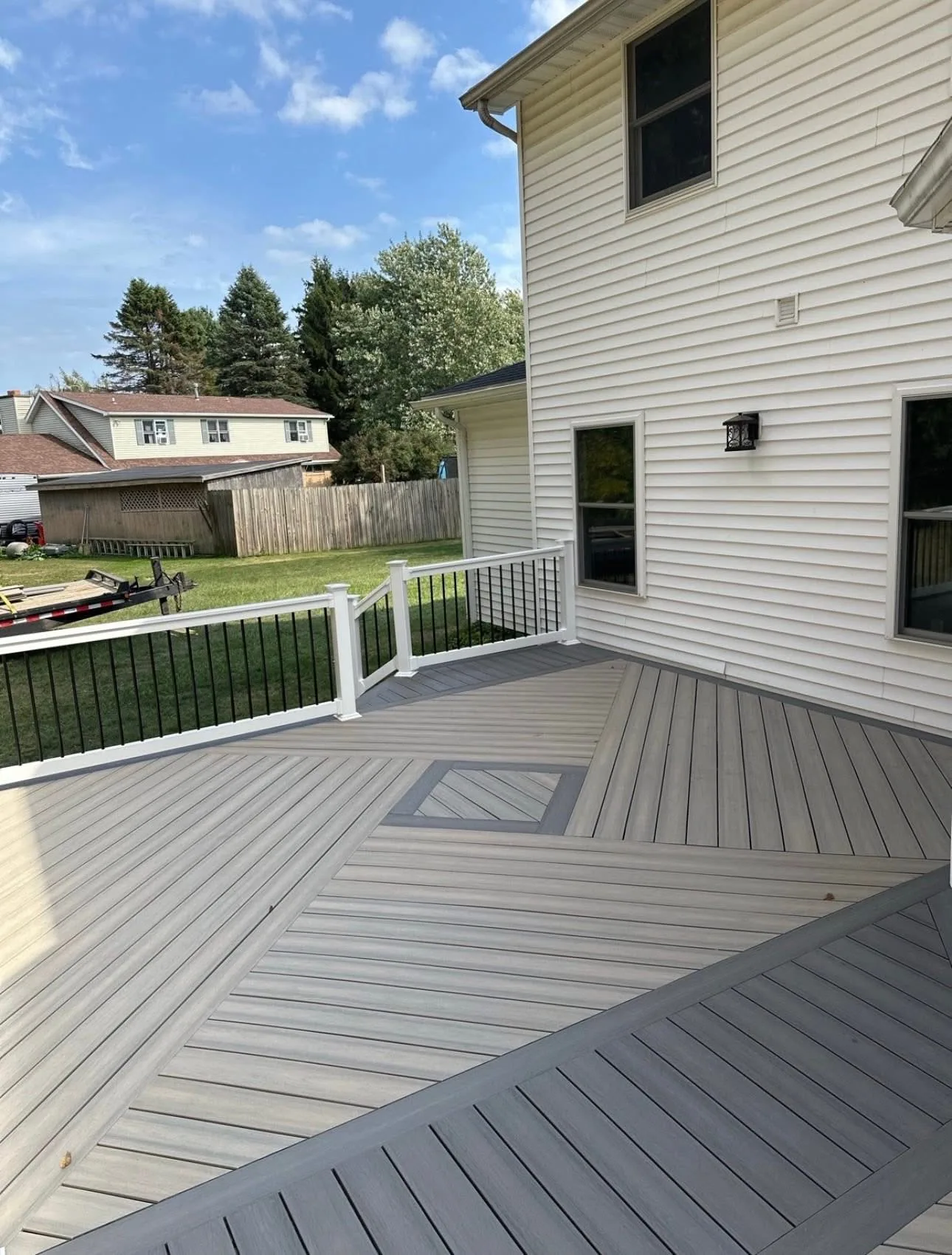 Grey composite deck with a square inlay and black border at a white sided home