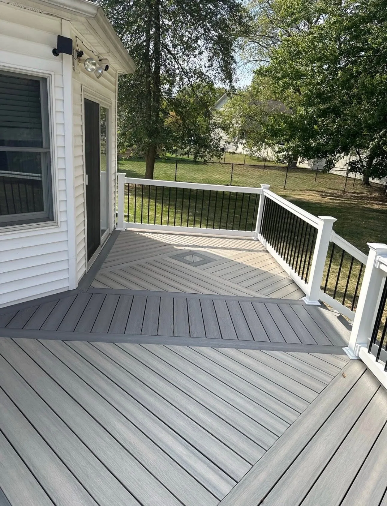 Grey composite deck with white railing and black balusters curving around a white home