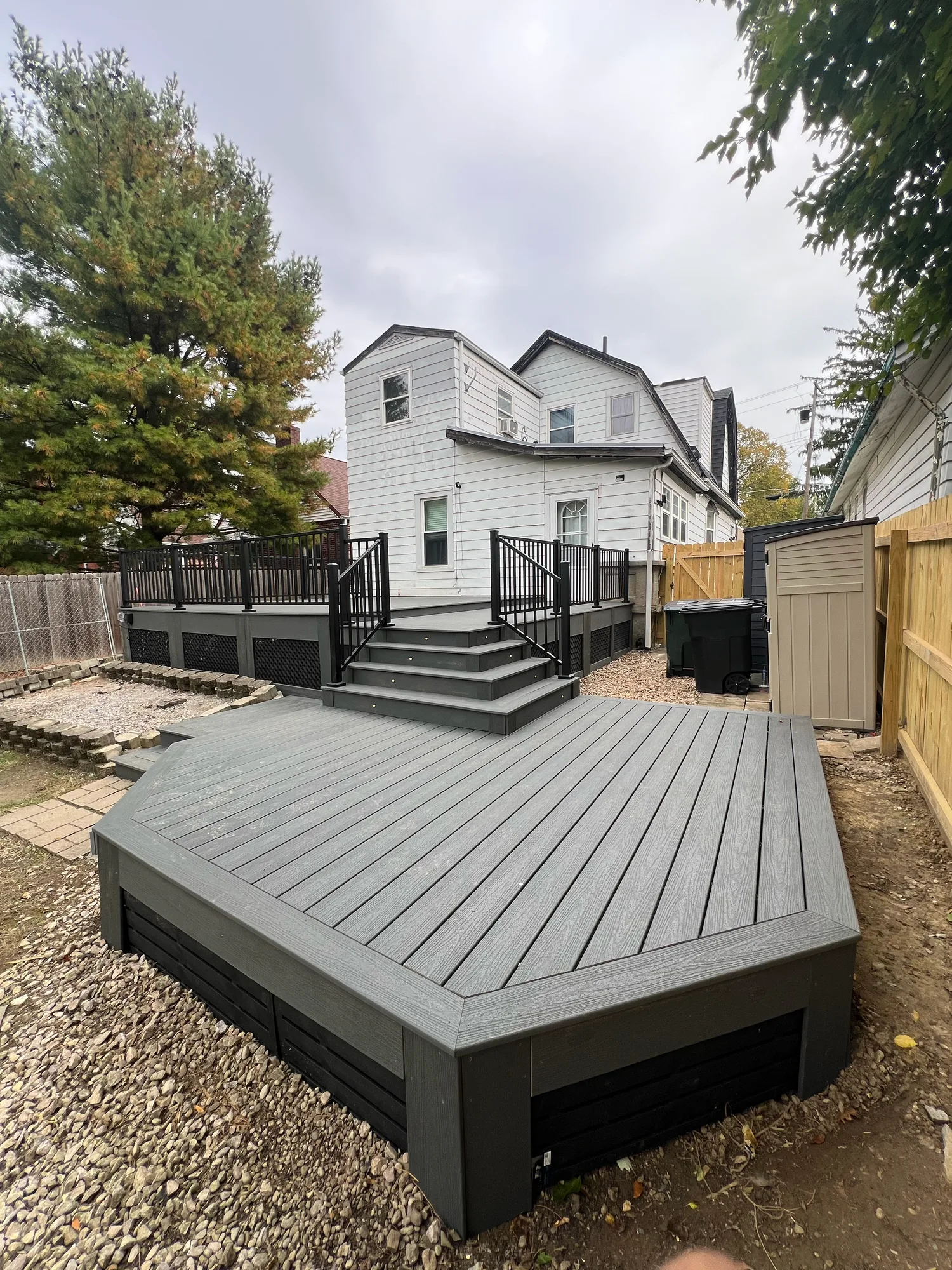 Grey composite platform deck with black skirting and steps in the yard of a white sided home