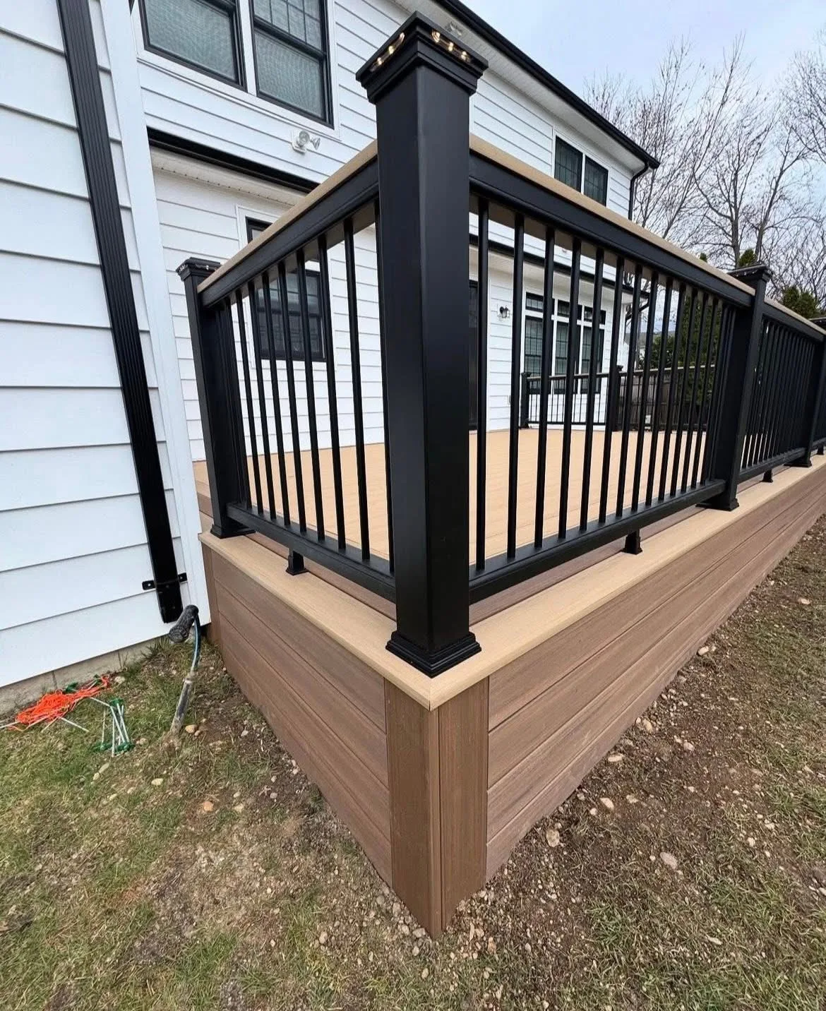 Black aluminum railing and post on a tan composite deck at a white sided home