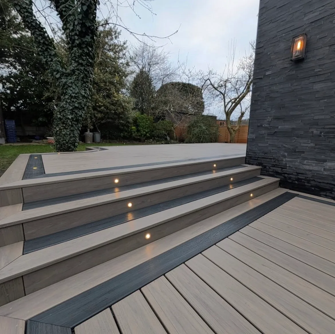 Grey composite steps with dark borders and small lights set into the risers beside a modern home