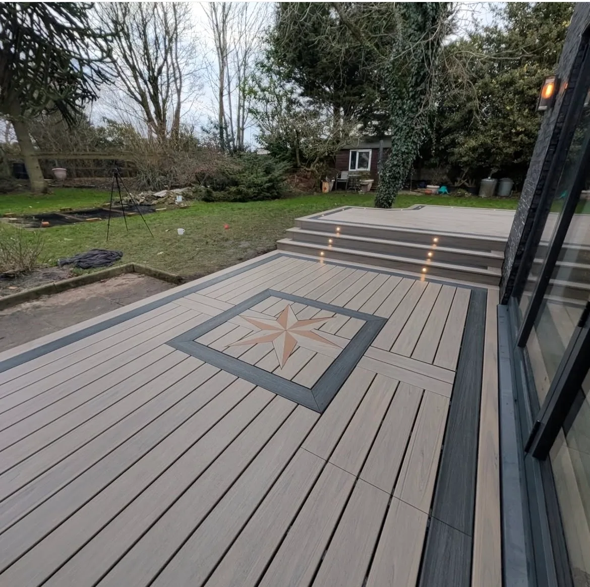 Composite deck with a star inlay and lights set into the steps at dusk beside a modern home