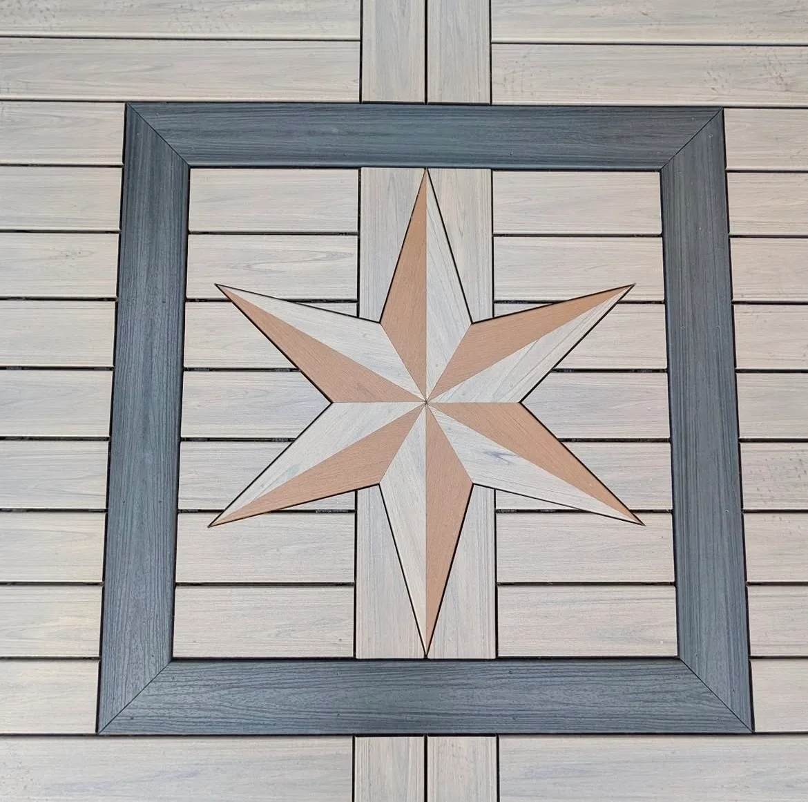 Close view of a compass star inlay set into composite deck boards with a dark square border
