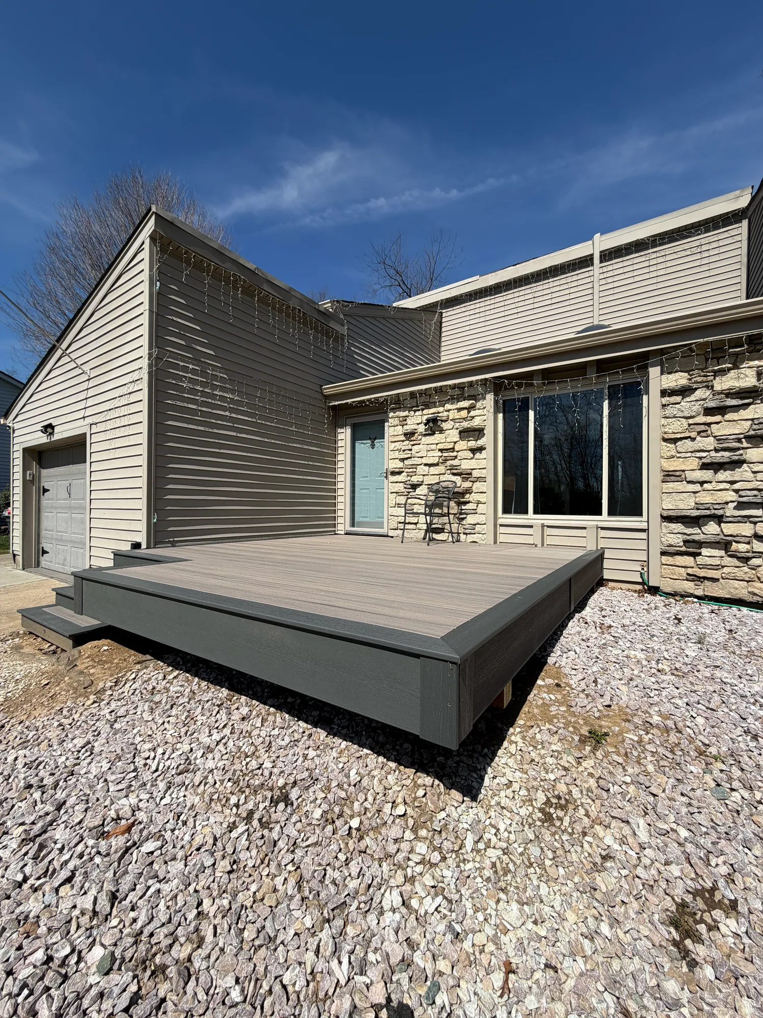 Low composite deck with black skirting at a home with stone and siding, set above a gravel border