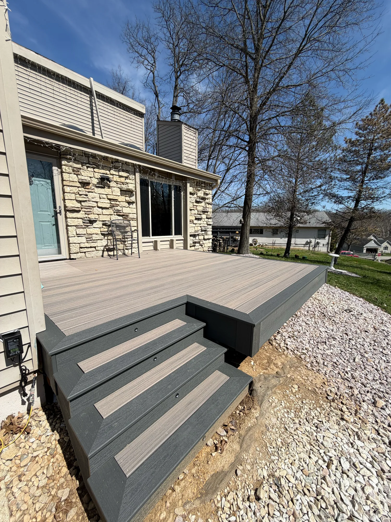 Grey composite deck with steps at a stone home above a fresh gravel and soil border