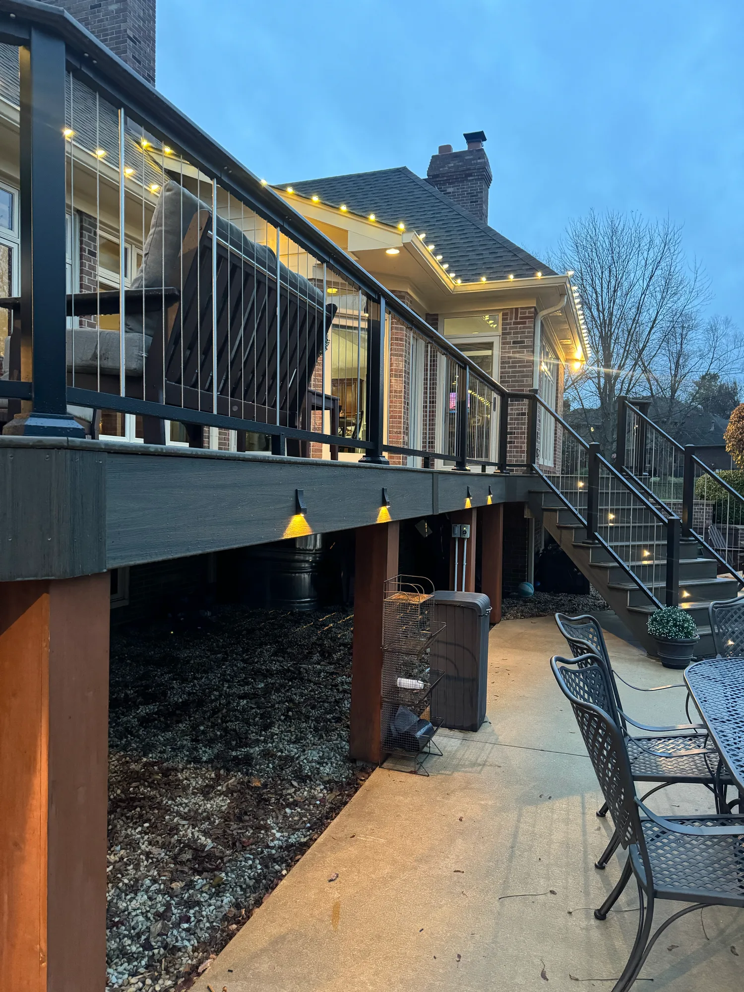 Elevated composite deck with string lights and lit stairs at dusk seen from the patio below