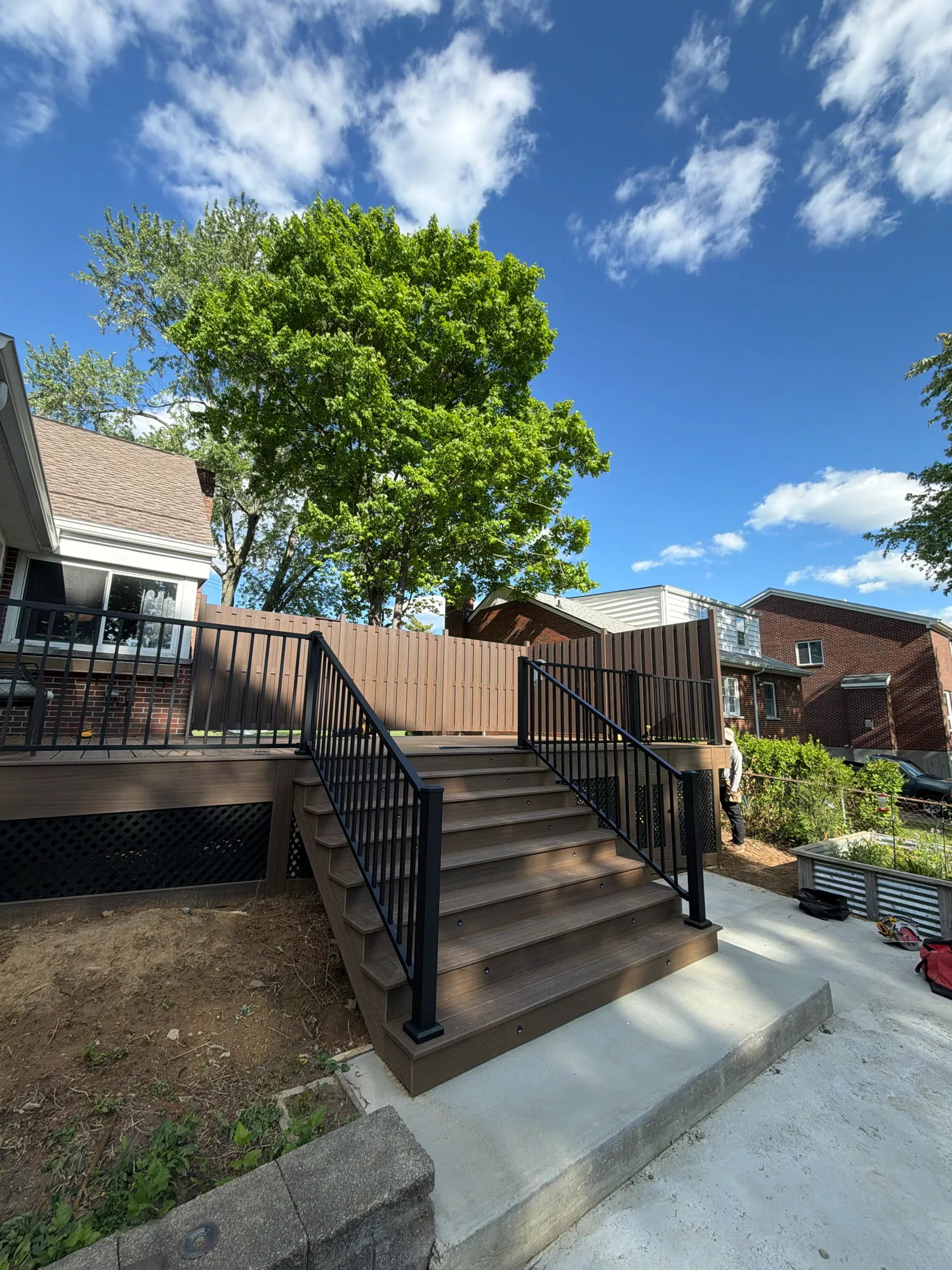 Brown composite deck with black railing and a staircase down to a concrete path under a blue sky