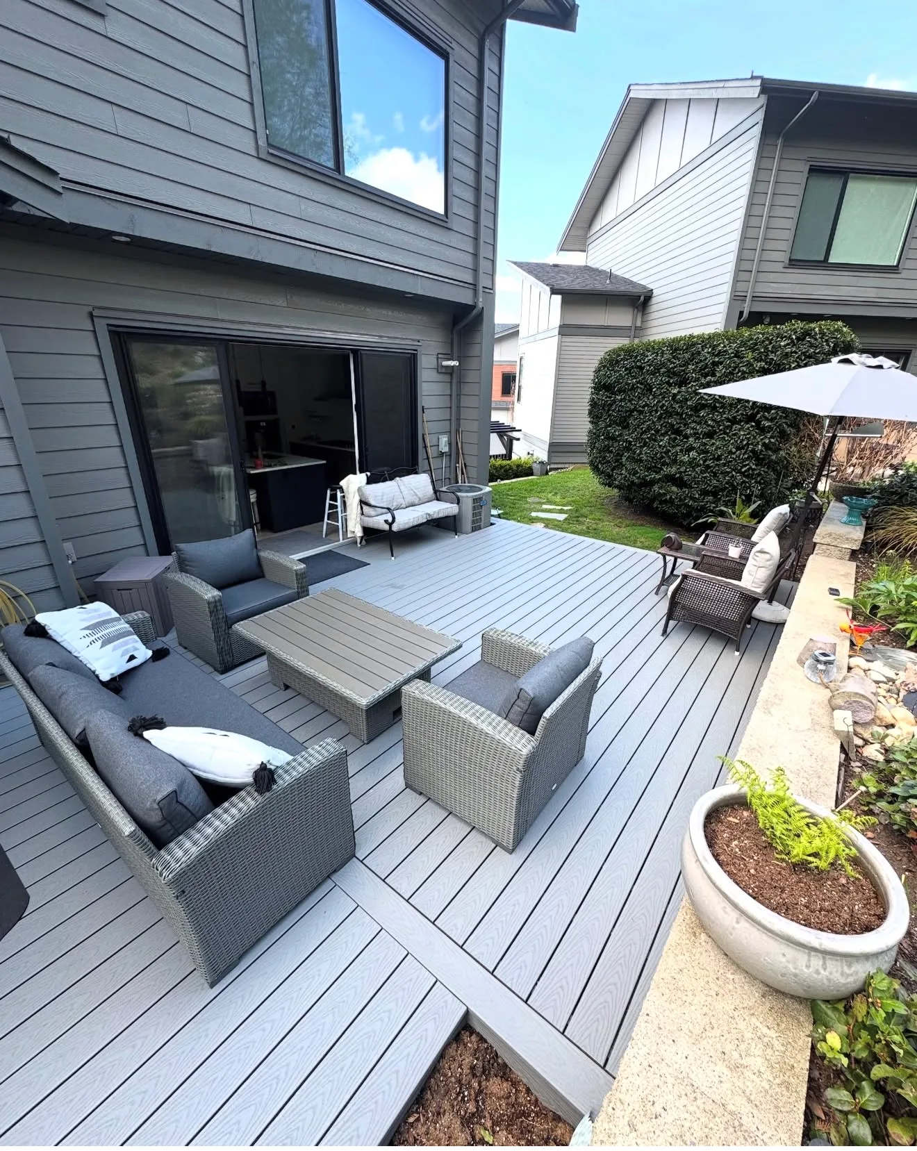 Grey composite deck with modern lounge furniture and an umbrella at a grey sided modern home