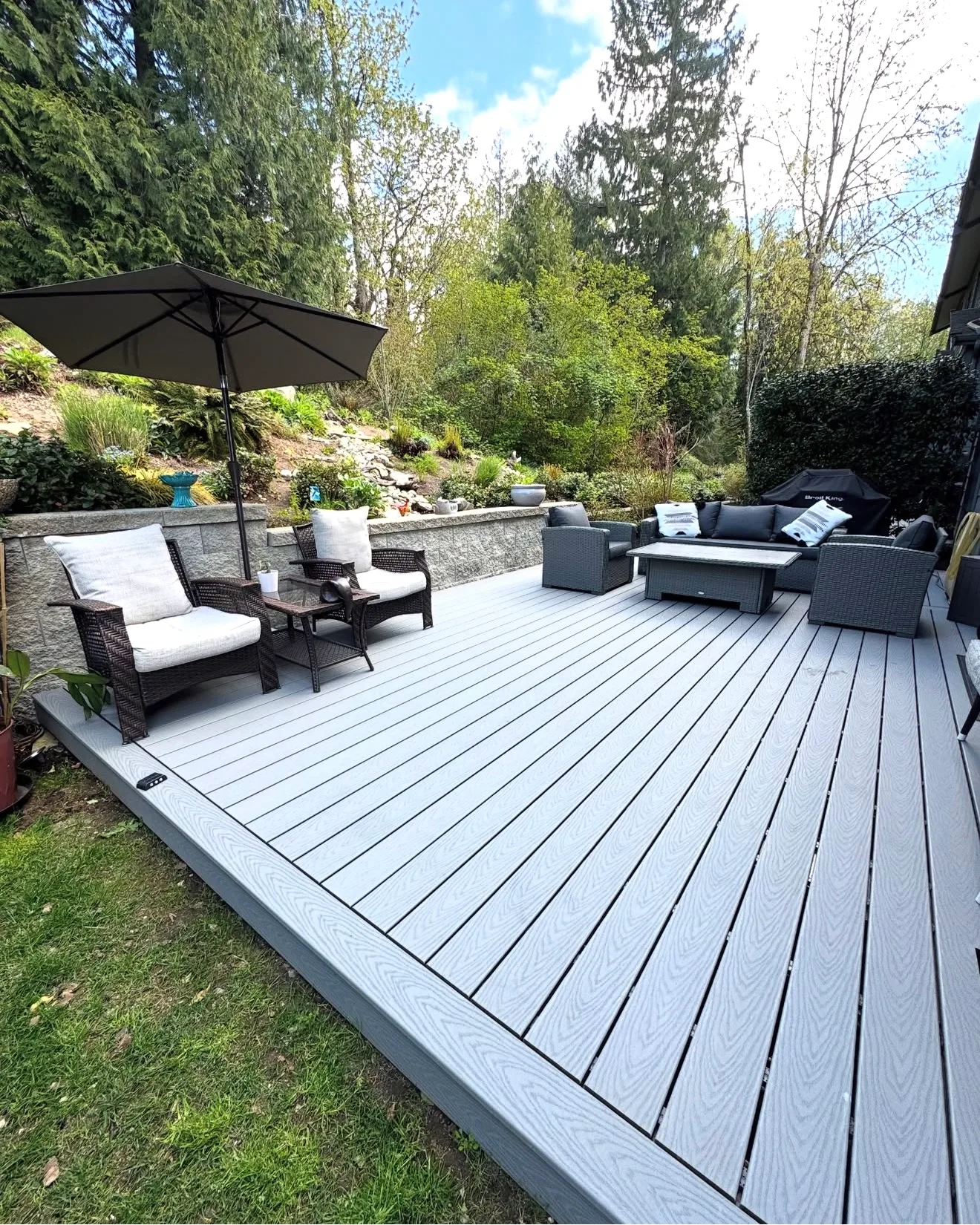 Grey composite deck with an umbrella and lounge seating on a hillside lot