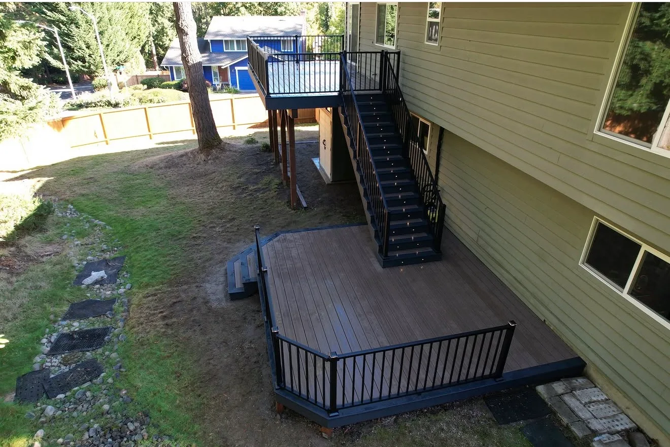 Aerial view of a grey composite deck with a black staircase climbing to an upper deck at a green sided home