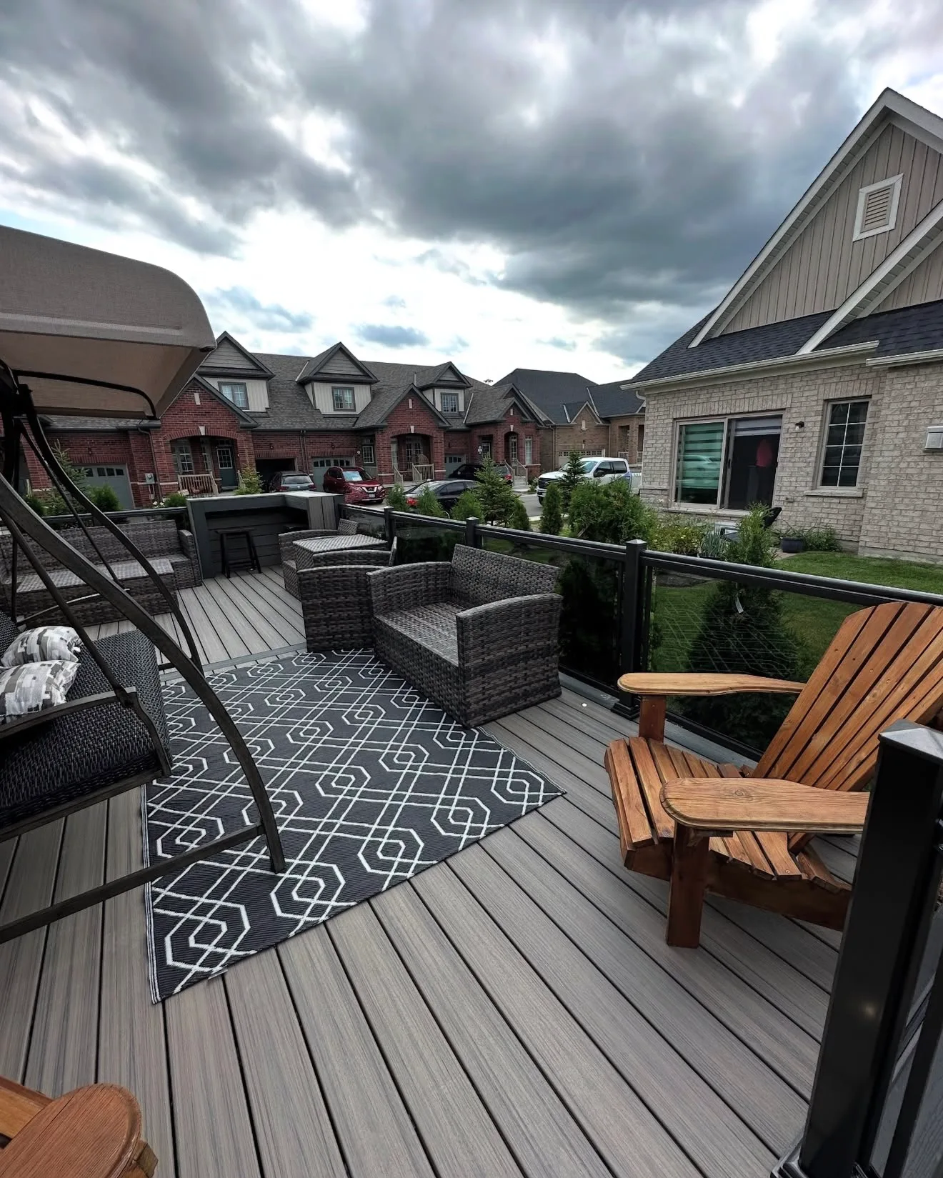 Grey composite deck with lounge furniture and an outdoor rug backing onto townhomes on an overcast day