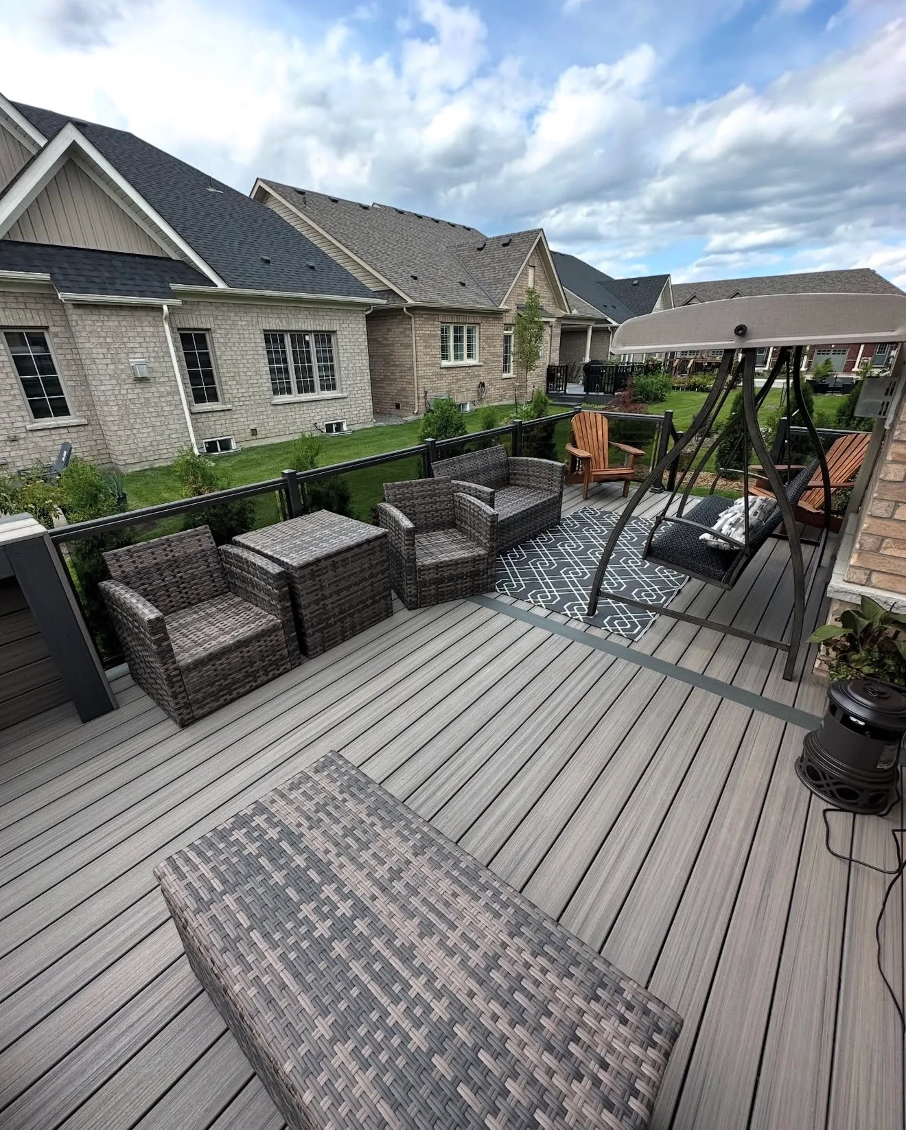 Grey composite deck with lounge chairs and a porch swing at a brick townhome