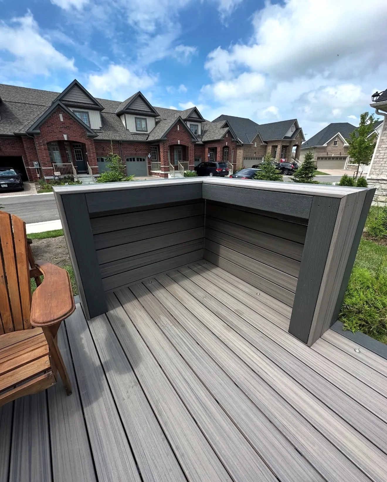 Grey composite deck with a built in wraparound bench and planter box behind townhomes