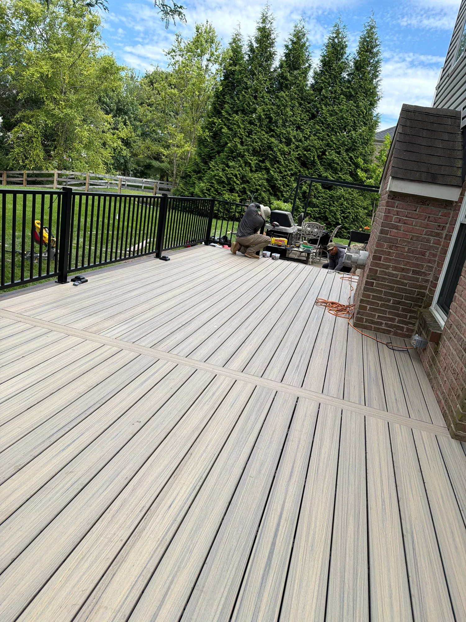 Light grey composite deck with black railing bordered by evergreen trees