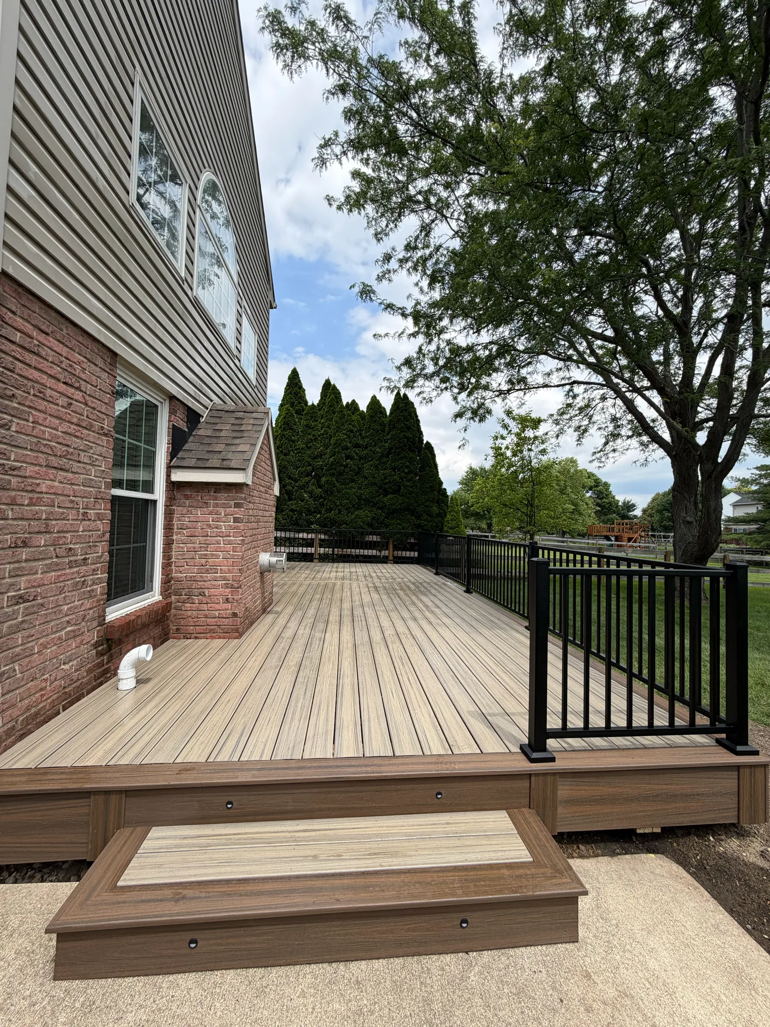 Brown composite deck with black railing and a wide step beside a brick home