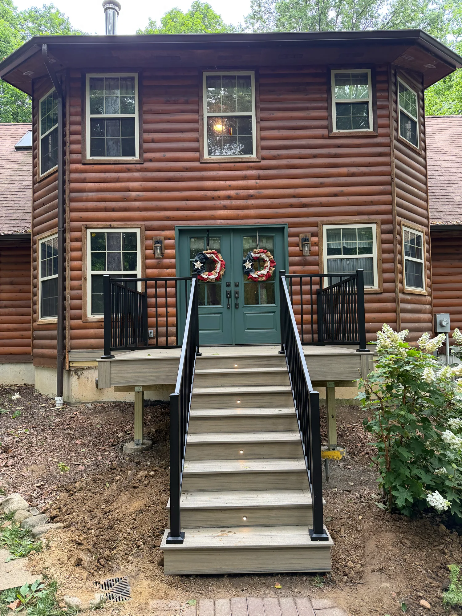 Composite steps with black railing leading up to the teal doors of a log cabin home