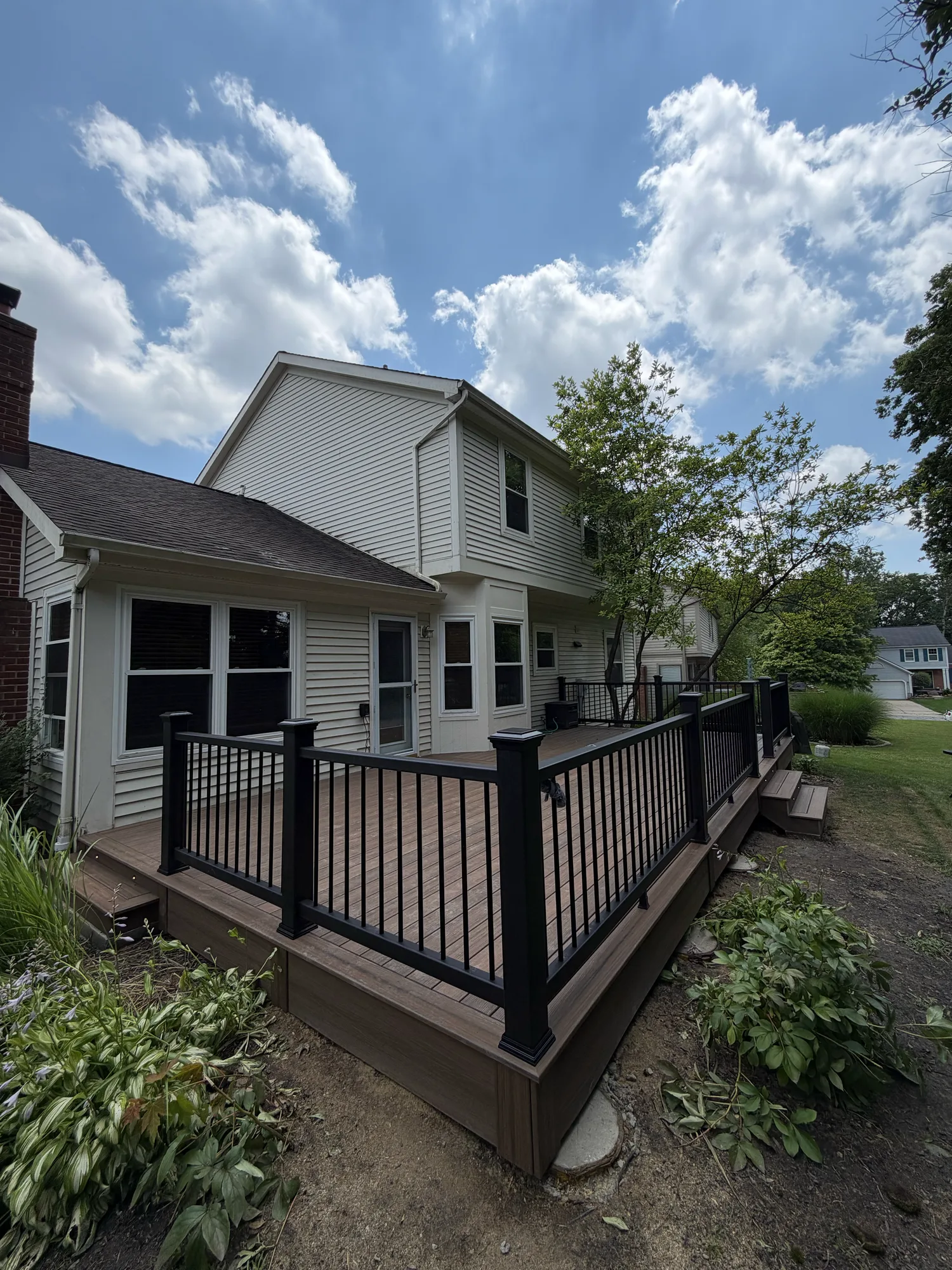 Brown composite deck with black railing at a white sided home under a blue sky