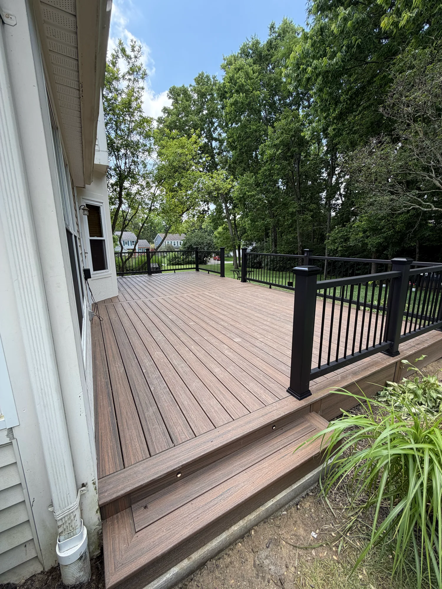 Brown composite deck with black railing running along a white sided home