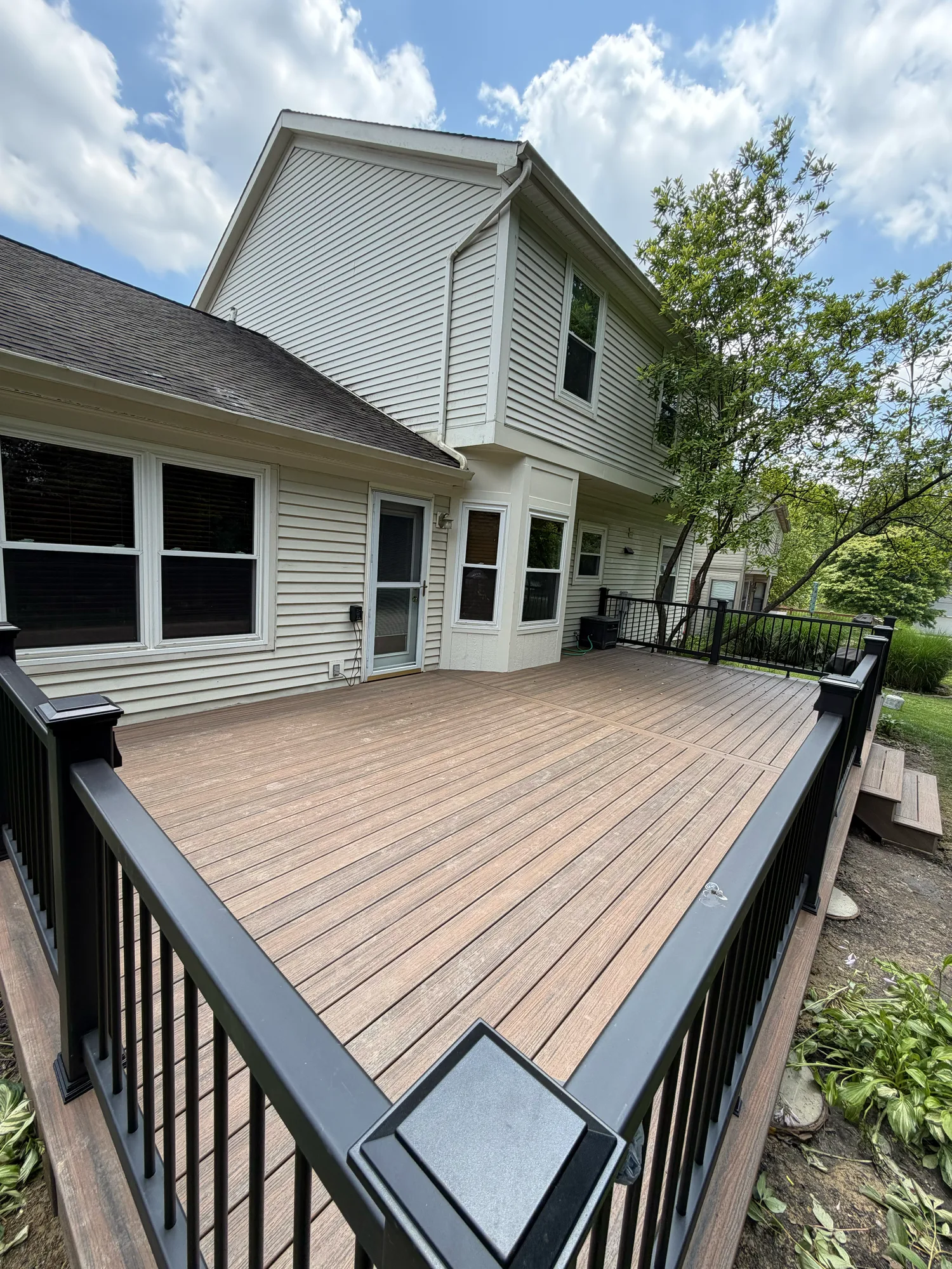 Brown composite deck with black railing at a white sided home surrounded by trees