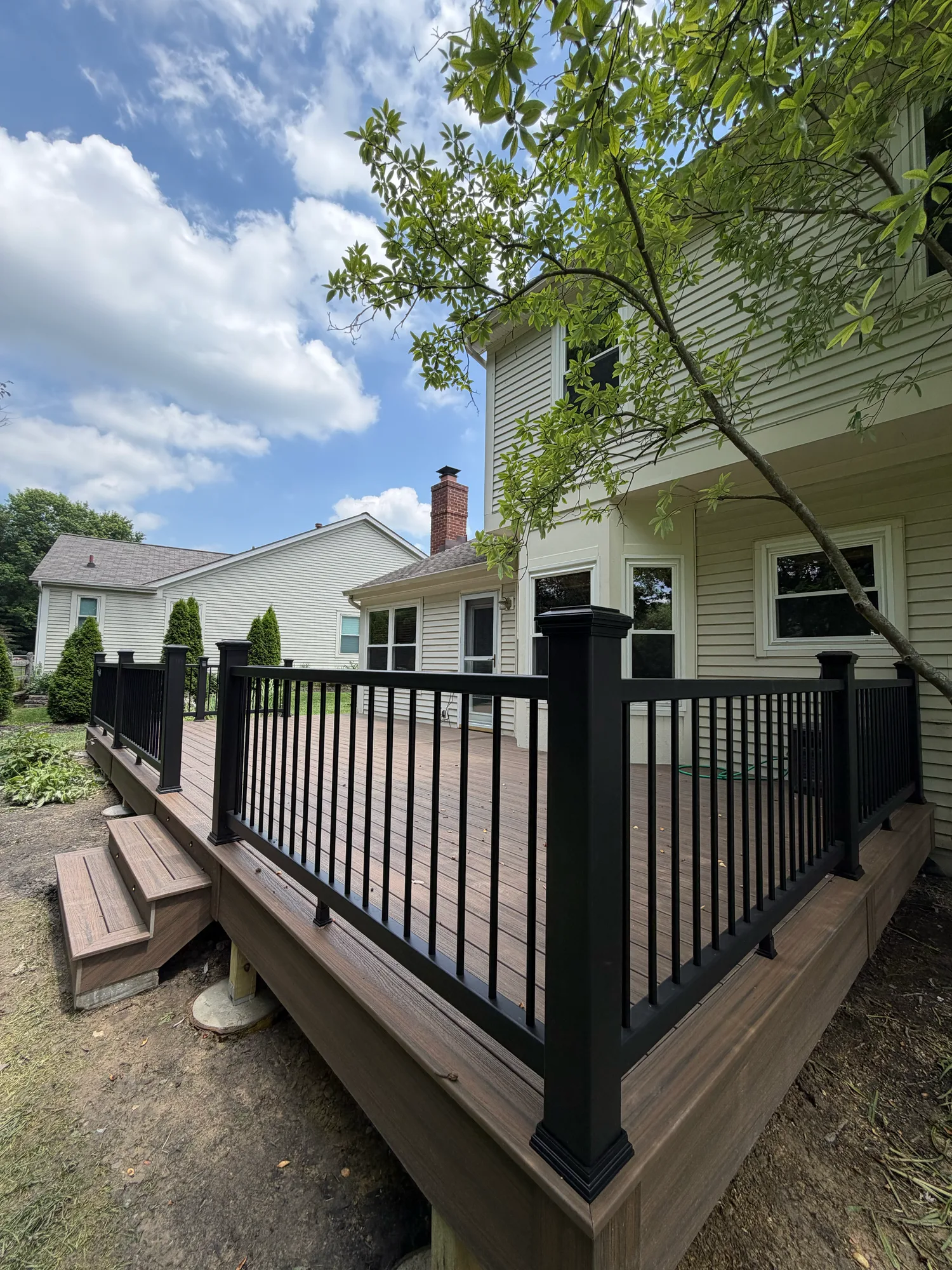Brown composite deck with black railing and steps at a green sided home
